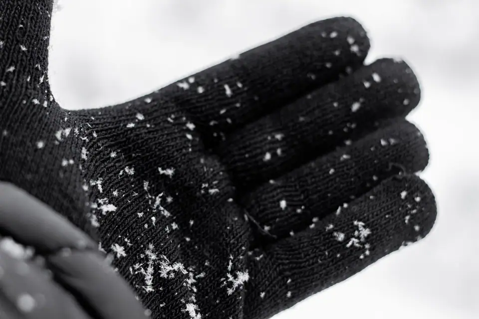 A black knit glove catching snowflakes during a snowfall