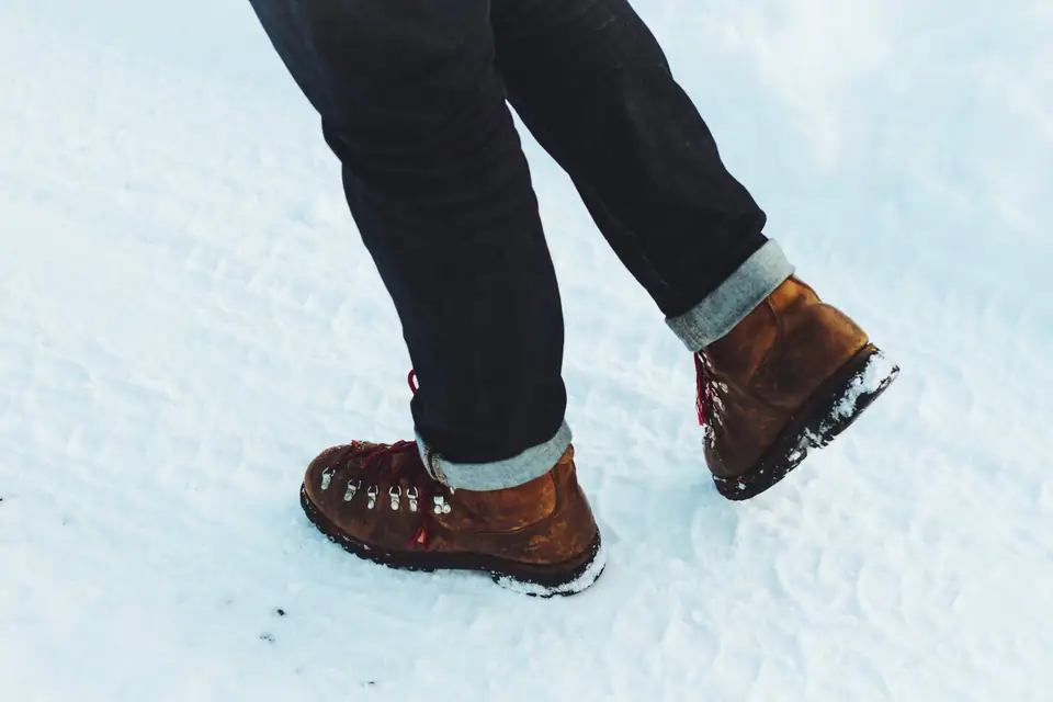 Brown leather lace-up boots and rolled jeans walking through snow
