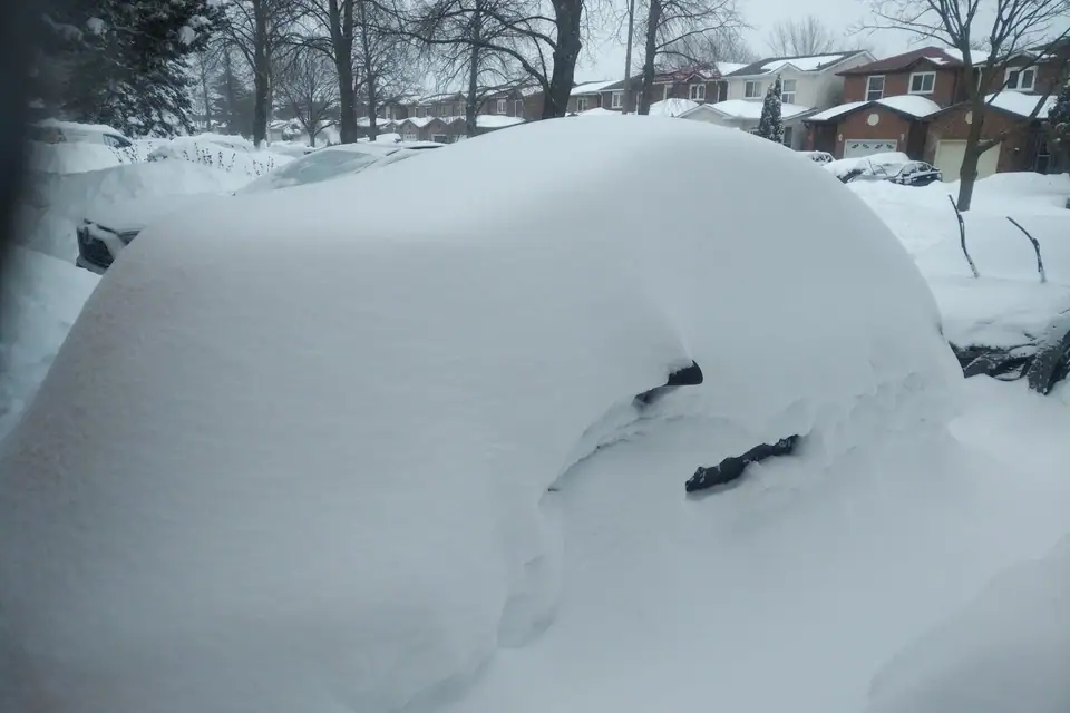 A parked car almost completely buried in snow on a residential street