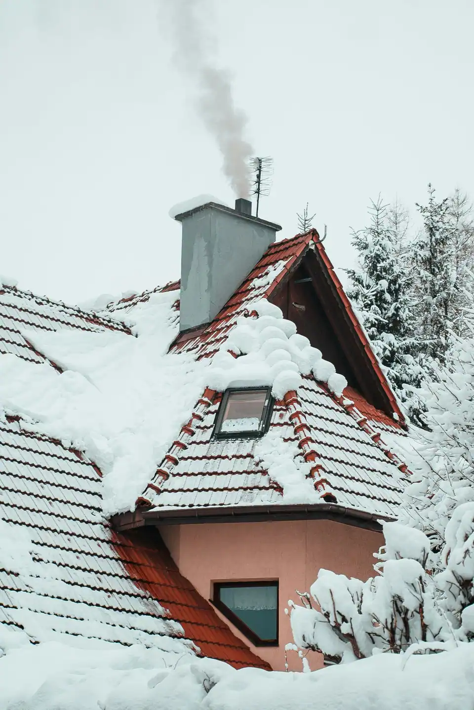 Smoke rising from a chimney on a snow-covered tiled roof