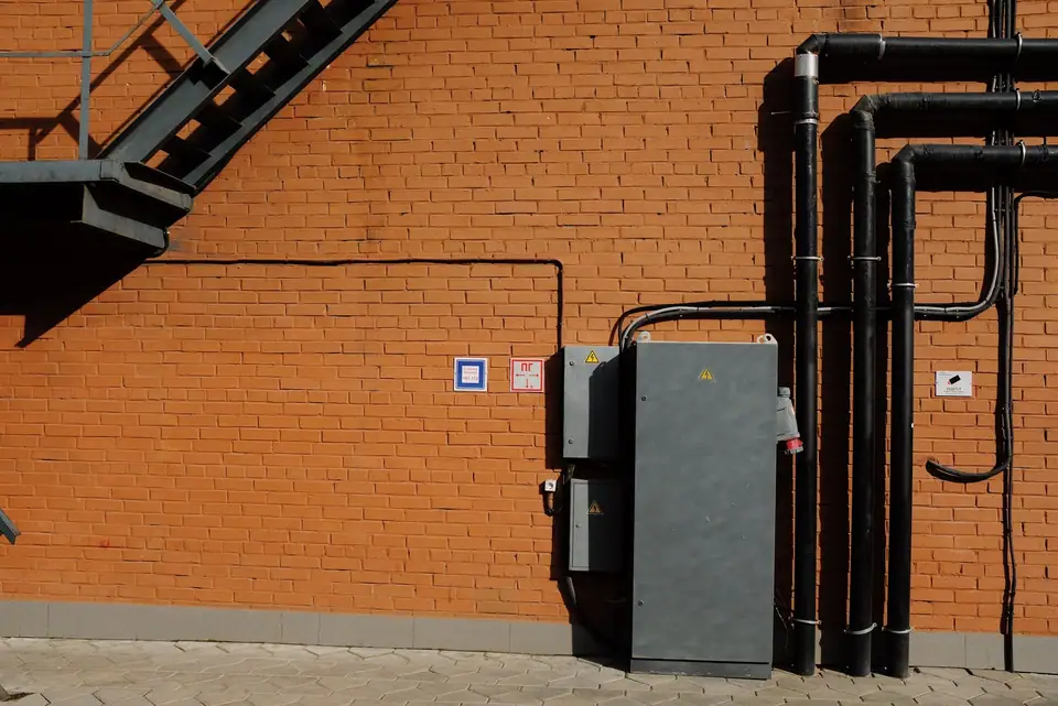 Gray outdoor electrical boxes and black conduit pipes mounted on a brick wall