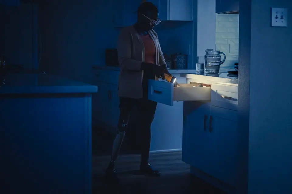 A person using a flashlight to search a kitchen drawer during a power outage