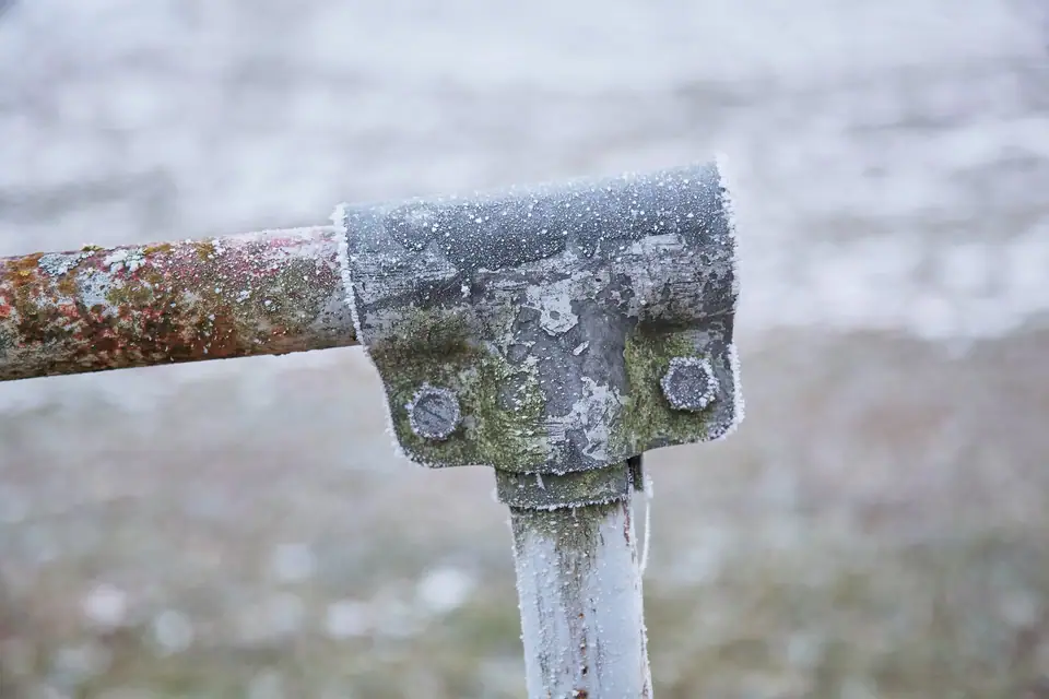 A frost-covered metal pipe joint outdoors on a freezing morning