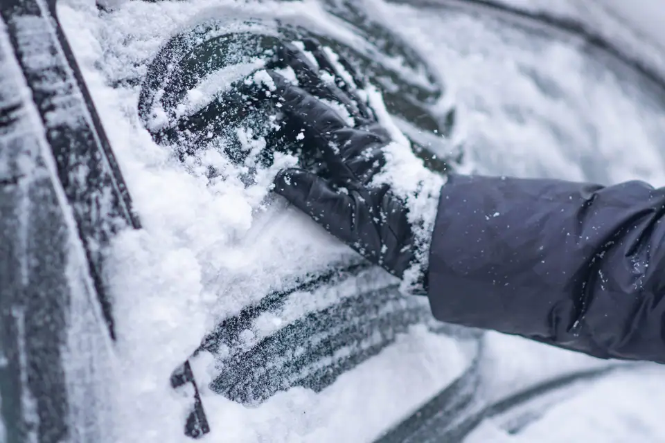A gloved hand brushing snow off a car window