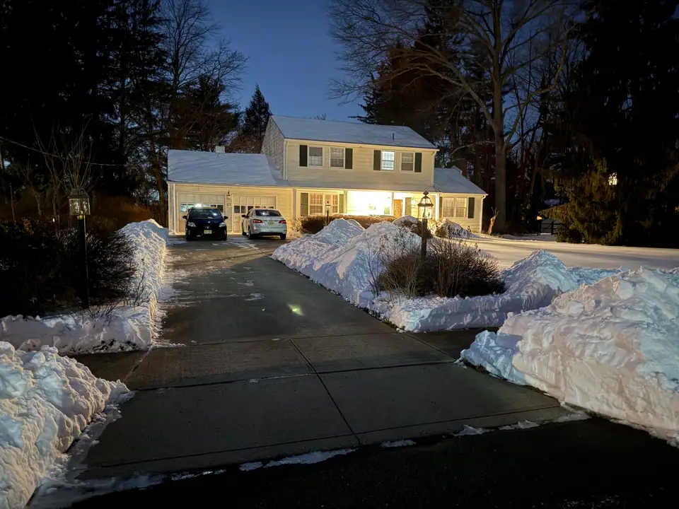 A house with a freshly shoveled driveway between snowbanks on the night after a winter storm
