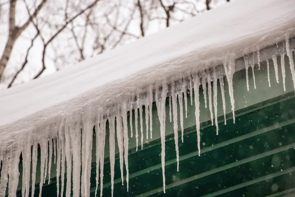 Thick snow and a row of icicles hanging from the edge of a roof after heavy snowfall