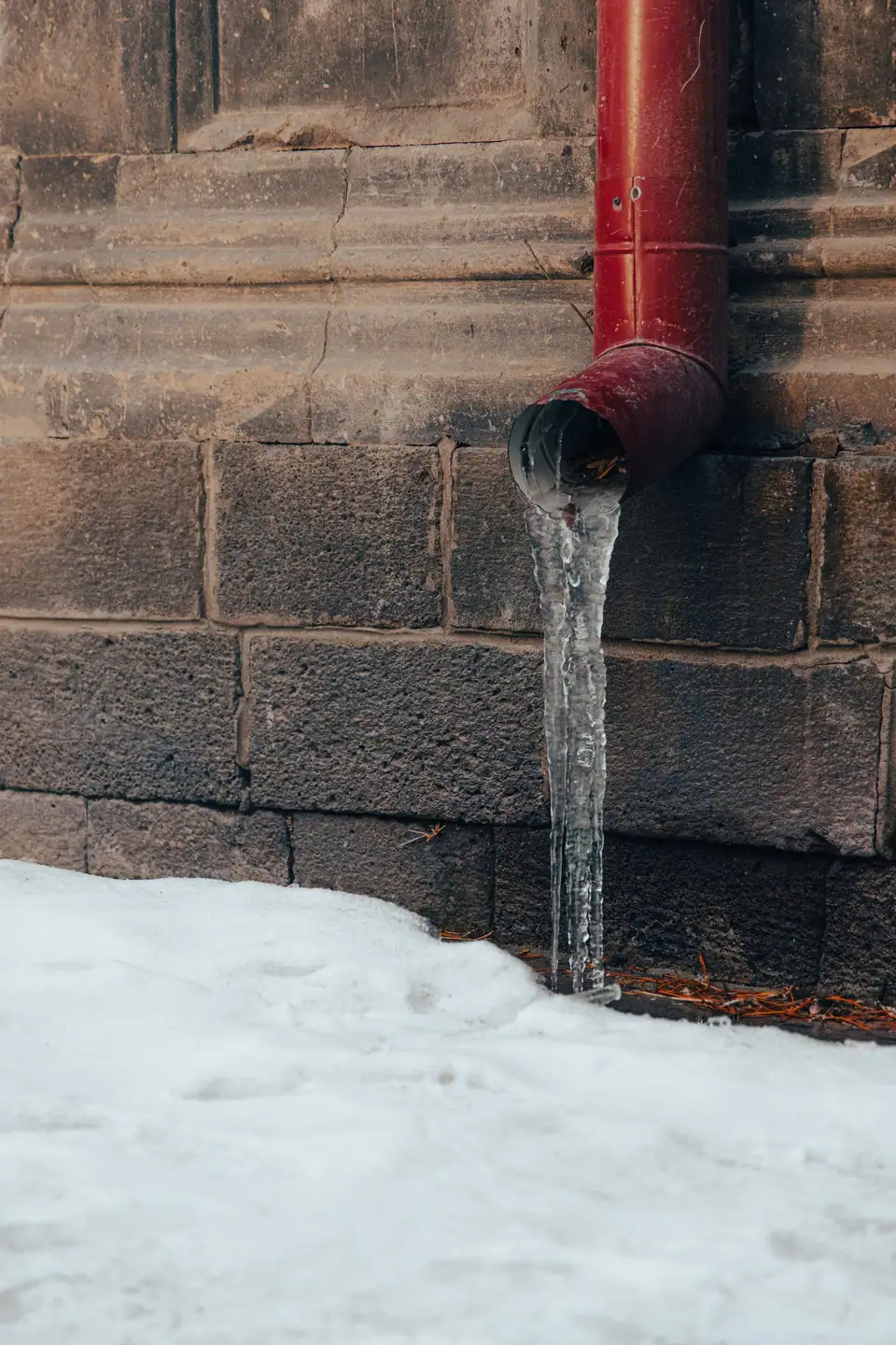 An exposed water pipe on a stone wall coated in ice with icicles hanging from it