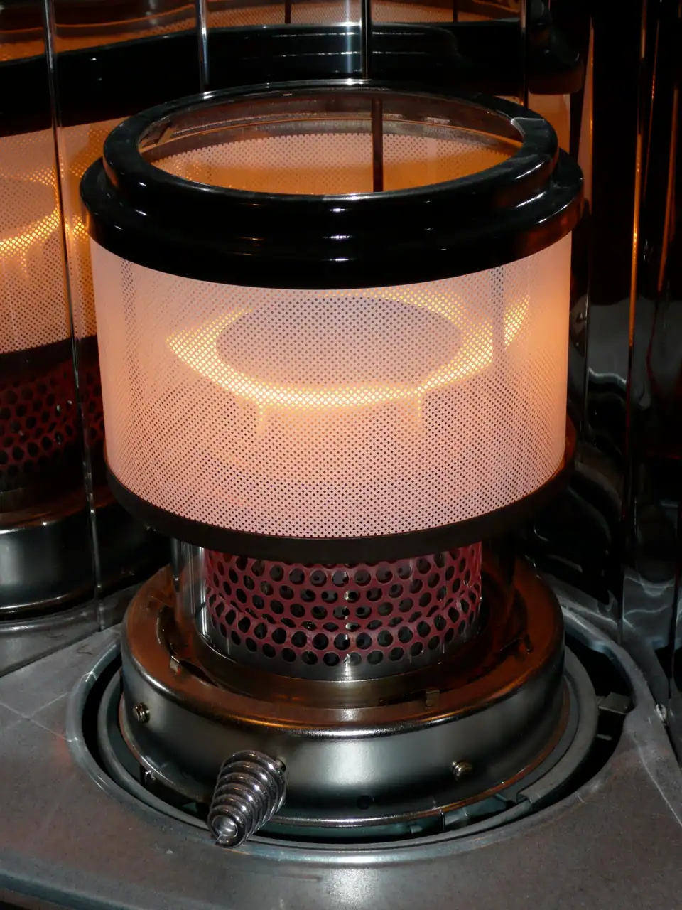 The glowing burner chimney of a lit kerosene heater, with a flame ring at its base