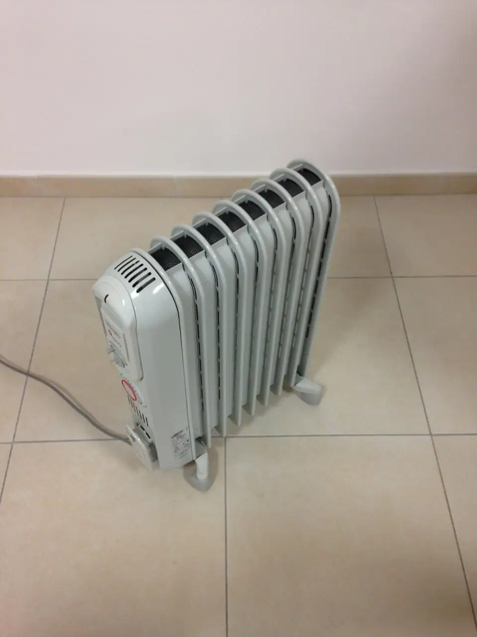 A white oil-filled radiator heater on casters standing on a tiled floor