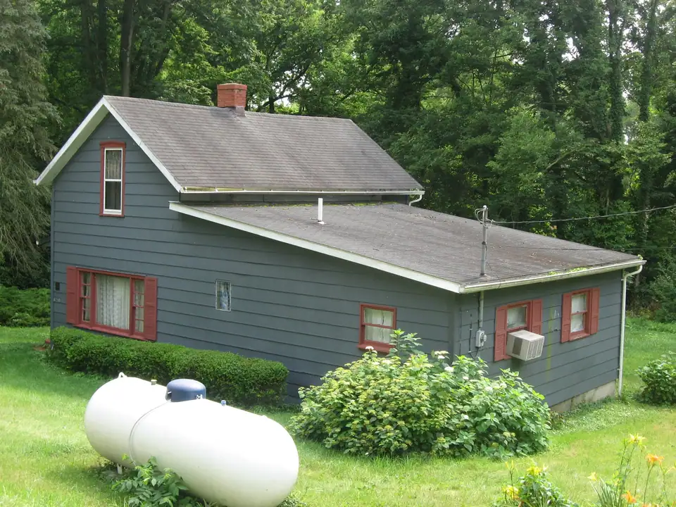 A white residential propane tank on the lawn beside a gray house