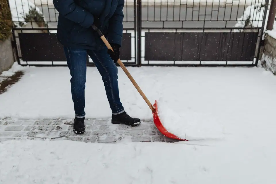 A person pushing snow off a paved path with a red shovel