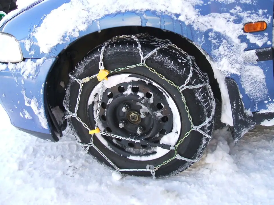 A snow chain fitted on the front wheel of a snowy car