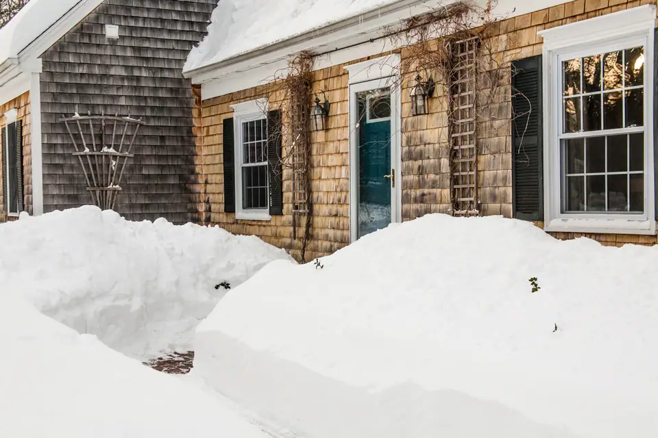Deep snow banked along a shoveled path to the front door of a shingled house