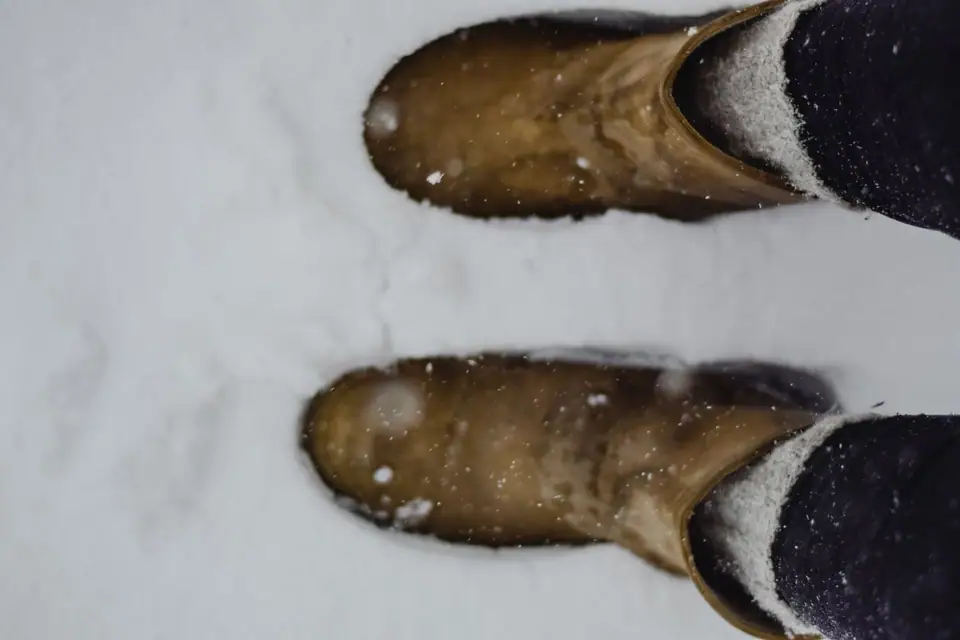 Two worn leather winter boots standing in fresh snow, seen from above